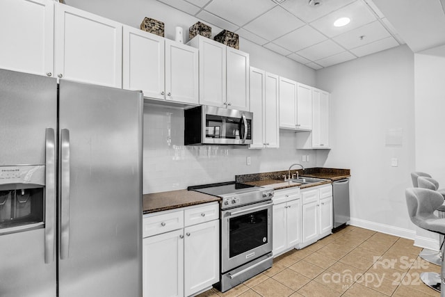 kitchen with a drop ceiling, sink, light tile patterned floors, white cabinetry, and stainless steel appliances