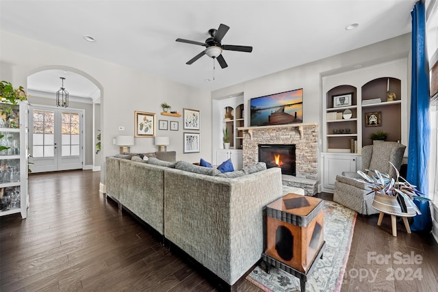 living room with built in shelves, ceiling fan, dark hardwood / wood-style flooring, a fireplace, and ornamental molding