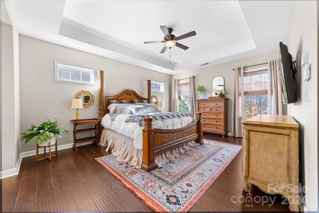 bedroom featuring ceiling fan, dark wood-type flooring, and a tray ceiling