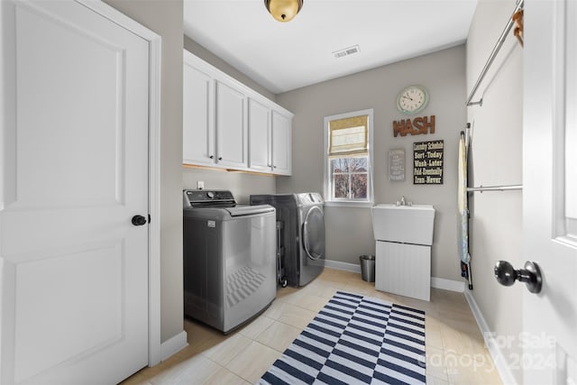 clothes washing area featuring cabinets, light tile patterned floors, and washing machine and clothes dryer