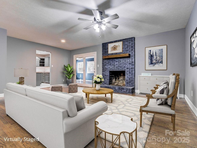 living room featuring a brick fireplace, dark wood-type flooring, a textured ceiling, and ceiling fan