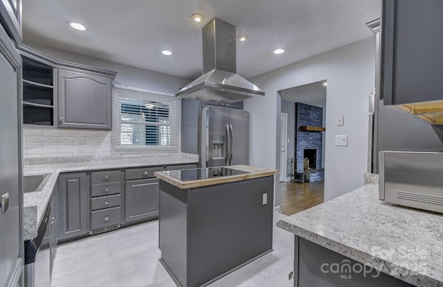 kitchen featuring a center island, stainless steel fridge, island range hood, a brick fireplace, and gray cabinetry