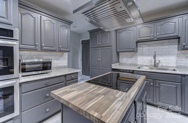 kitchen featuring wall chimney range hood, decorative backsplash, sink, wood counters, and black electric cooktop