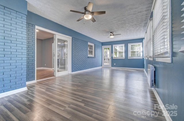 unfurnished living room featuring ceiling fan, dark hardwood / wood-style flooring, brick wall, and a textured ceiling