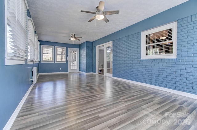 unfurnished living room featuring brick wall, a textured ceiling, radiator, hardwood / wood-style floors, and ceiling fan