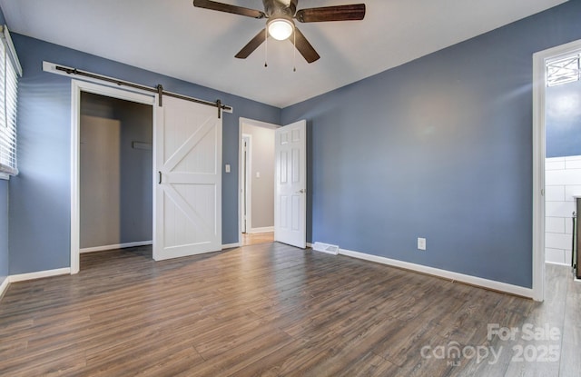 unfurnished bedroom with ceiling fan, dark hardwood / wood-style flooring, and a barn door