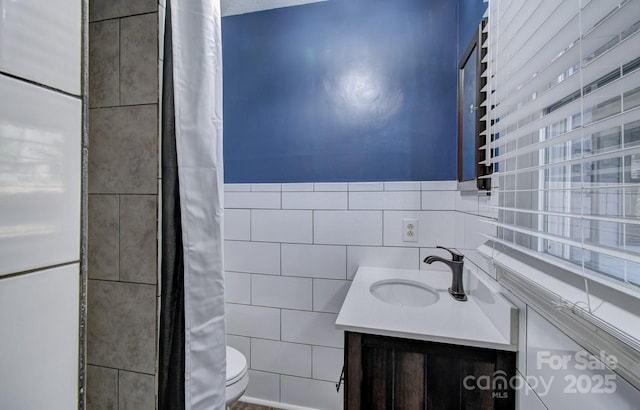 bathroom with toilet, vanity, and tile walls