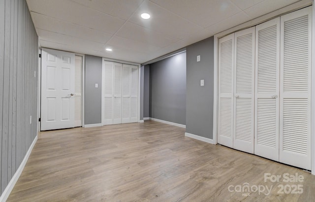 unfurnished bedroom featuring multiple closets, light hardwood / wood-style floors, a drop ceiling, and wooden walls