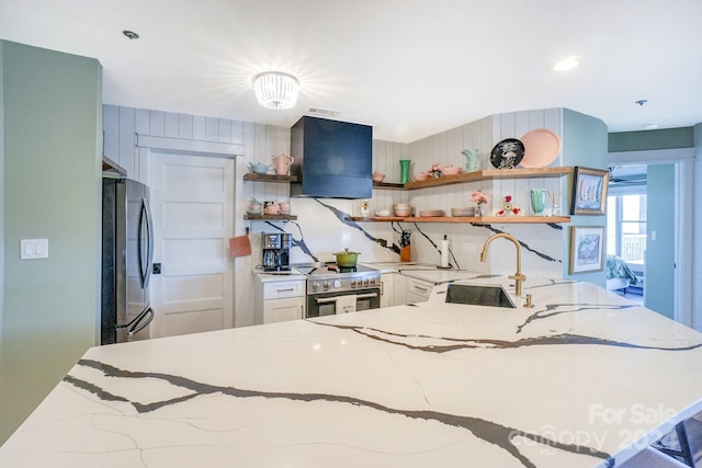 kitchen featuring appliances with stainless steel finishes, light stone counters, sink, white cabinets, and range hood