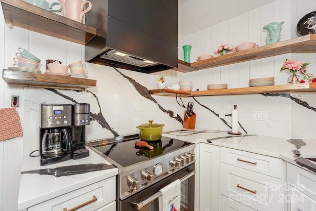 kitchen with white cabinetry, high end range, light stone counters, and range hood