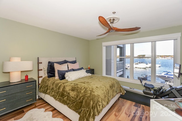 bedroom with hardwood / wood-style floors, ceiling fan, and a water view