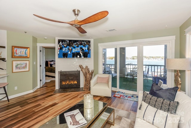 living room featuring a tiled fireplace, ceiling fan, wood finished floors, and a healthy amount of sunlight