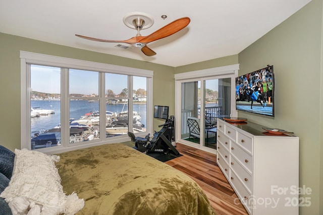 bedroom with access to outside, ceiling fan, wood finished floors, a water view, and visible vents