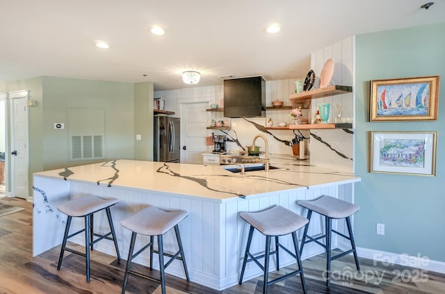 kitchen with visible vents, open shelves, freestanding refrigerator, a peninsula, and wall chimney exhaust hood