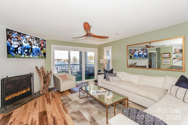 living room featuring ceiling fan, a lit fireplace, and wood finished floors