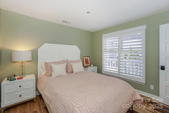bedroom with baseboards, multiple windows, wood finished floors, and visible vents