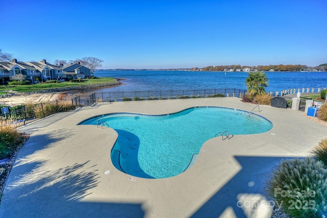 community pool featuring fence, a patio, and a water view