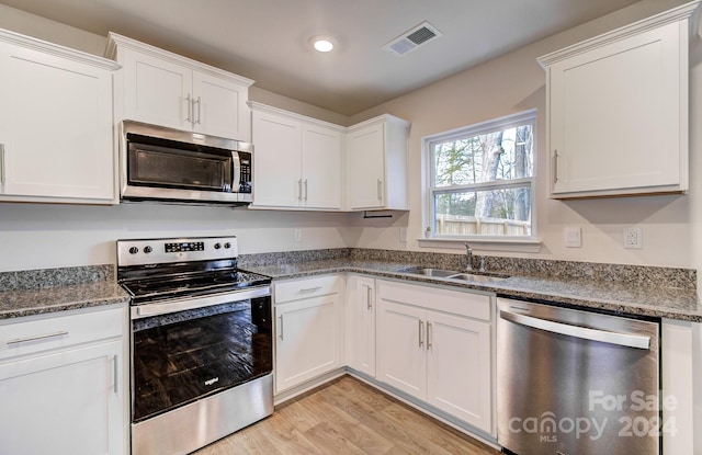 kitchen with white cabinets, sink, dark stone countertops, light wood-type flooring, and stainless steel appliances