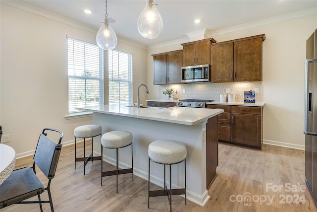 kitchen with sink, hanging light fixtures, an island with sink, appliances with stainless steel finishes, and light wood-type flooring