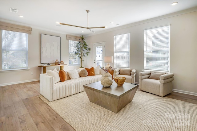 living room with light wood-type flooring, plenty of natural light, ornamental molding, and a notable chandelier