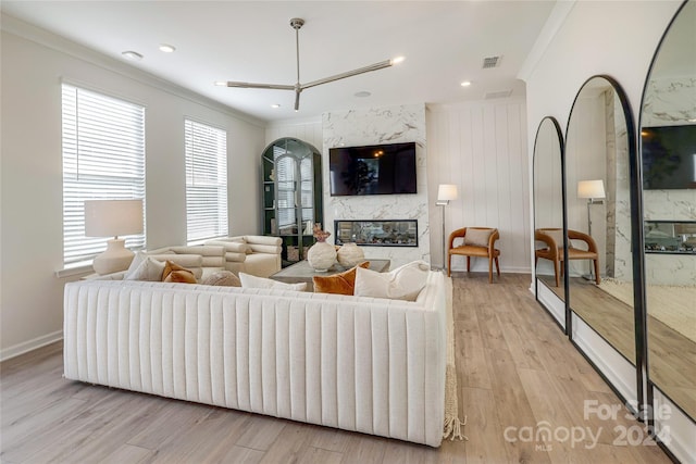 living room with wood walls, light wood-type flooring, crown molding, and a high end fireplace