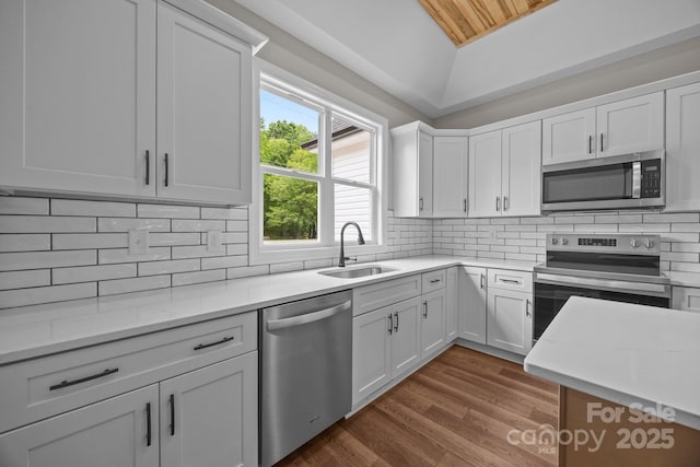 kitchen with dark wood-style flooring, white cabinets, a sink, appliances with stainless steel finishes, and vaulted ceiling