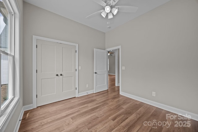 unfurnished bedroom featuring a closet, baseboards, a ceiling fan, and light wood-style flooring