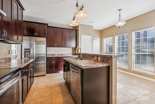 kitchen featuring sink, hanging light fixtures, light tile patterned floors, an island with sink, and appliances with stainless steel finishes