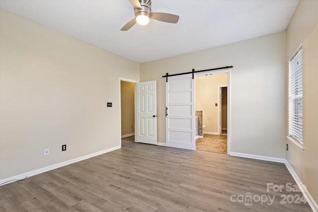 unfurnished bedroom featuring a barn door, light hardwood / wood-style flooring, and ceiling fan