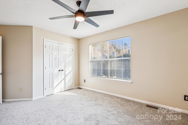 unfurnished bedroom with ceiling fan, a closet, light colored carpet, and a textured ceiling