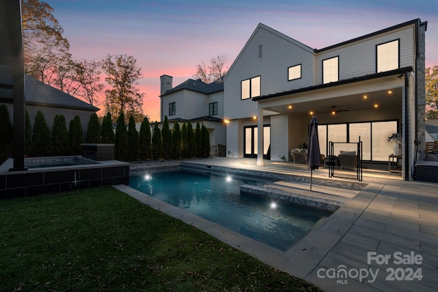 pool at dusk with a patio area, an in ground hot tub, a yard, and ceiling fan