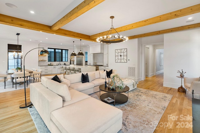 living room with beamed ceiling, a notable chandelier, and light hardwood / wood-style flooring