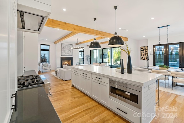 kitchen featuring hanging light fixtures, beam ceiling, light hardwood / wood-style flooring, white cabinets, and stainless steel microwave