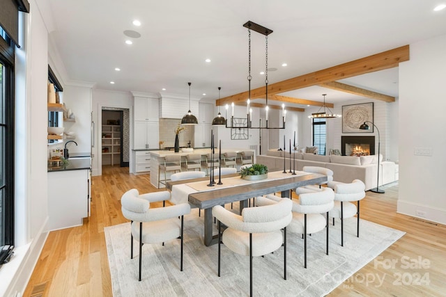 dining space with a large fireplace, light hardwood / wood-style floors, ornamental molding, and sink