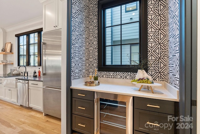 bar with white cabinets, ornamental molding, light hardwood / wood-style floors, stainless steel appliances, and beverage cooler