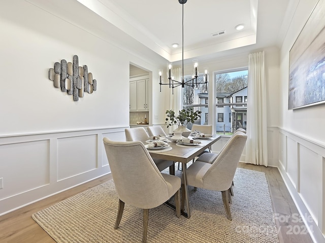 dining area featuring a raised ceiling, light hardwood / wood-style flooring, and a notable chandelier