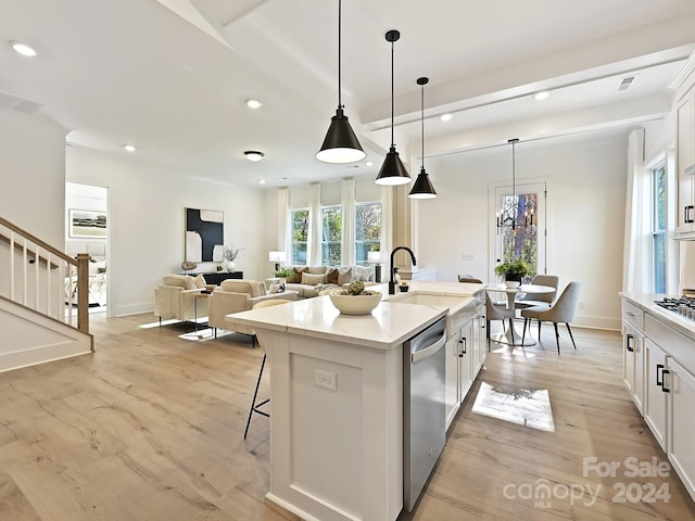 kitchen with stainless steel dishwasher, decorative light fixtures, a kitchen island with sink, white cabinets, and light wood-type flooring