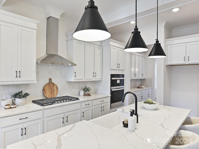 kitchen featuring light stone countertops, appliances with stainless steel finishes, wall chimney range hood, pendant lighting, and white cabinets