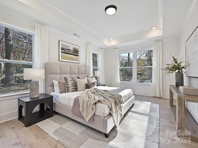 bedroom with a raised ceiling and light wood-type flooring