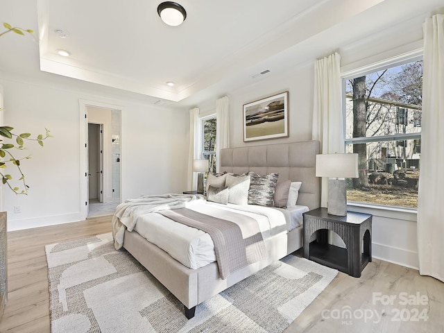 bedroom with a raised ceiling, light wood-type flooring, and multiple windows