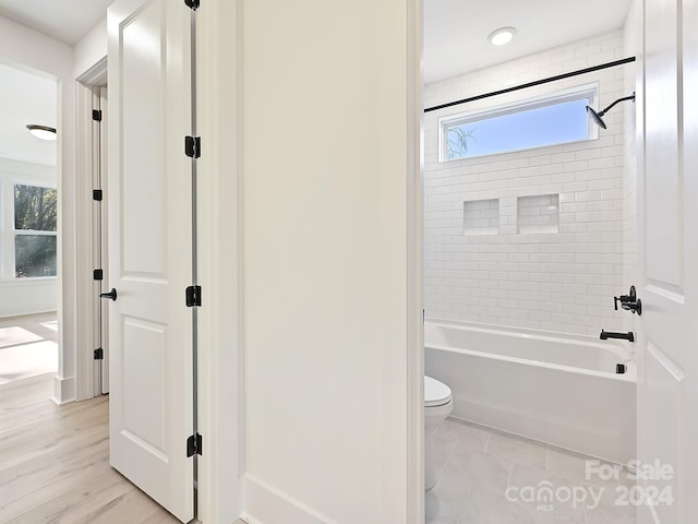 bathroom with hardwood / wood-style flooring, tiled shower / bath combo, and toilet