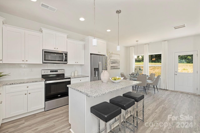 kitchen featuring a kitchen breakfast bar, light wood-type flooring, stainless steel appliances, white cabinets, and hanging light fixtures