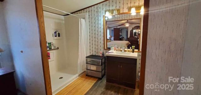 bathroom featuring a stall shower, wallpapered walls, ensuite bathroom, and wood finished floors