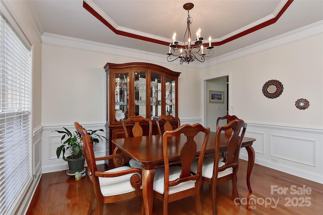 dining space with a raised ceiling, dark hardwood / wood-style floors, an inviting chandelier, and crown molding