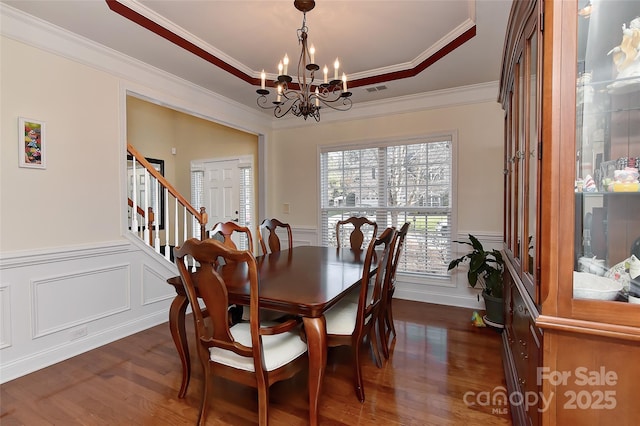 dining space featuring a raised ceiling, an inviting chandelier, dark wood-type flooring, and ornamental molding