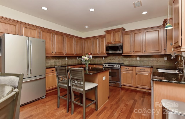 kitchen with sink, hanging light fixtures, a breakfast bar, a kitchen island, and appliances with stainless steel finishes