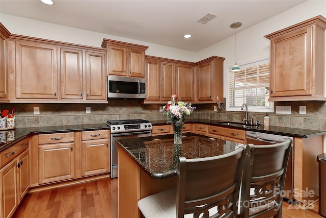 kitchen featuring a kitchen bar, stainless steel appliances, sink, a kitchen island, and hanging light fixtures