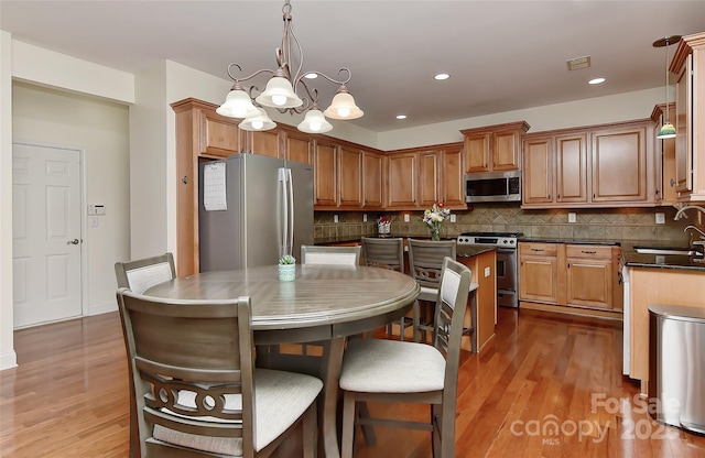 kitchen with appliances with stainless steel finishes, sink, a notable chandelier, a kitchen island, and hanging light fixtures