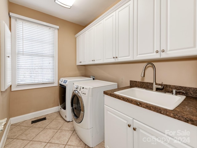 clothes washing area with washing machine and clothes dryer, cabinets, sink, and a healthy amount of sunlight