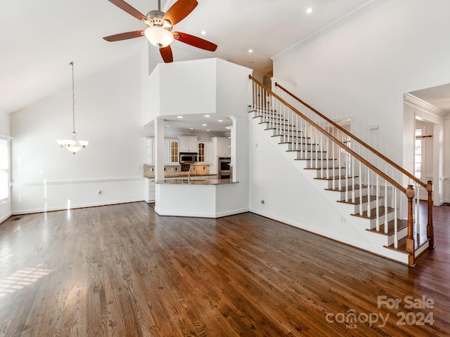 unfurnished living room with high vaulted ceiling, ceiling fan with notable chandelier, sink, crown molding, and dark hardwood / wood-style floors